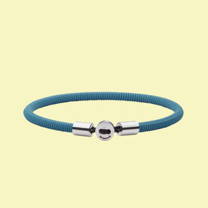 The Smile bracelet in Teal Blue Silicon Rubber with stainless steel button clasp. Fully waterproof. Yellow background.