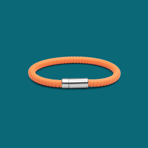The Signature 幸运168飞艇开奖官网开奖 in orange with stainless steel clasp. FKM fluoroelastomer rubber – Fully waterproof. Blue/Green background.